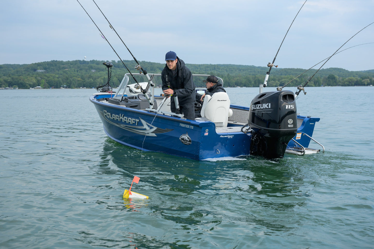 Two people on a blue fishing boat with a Suzuki 115 motor on a lake.