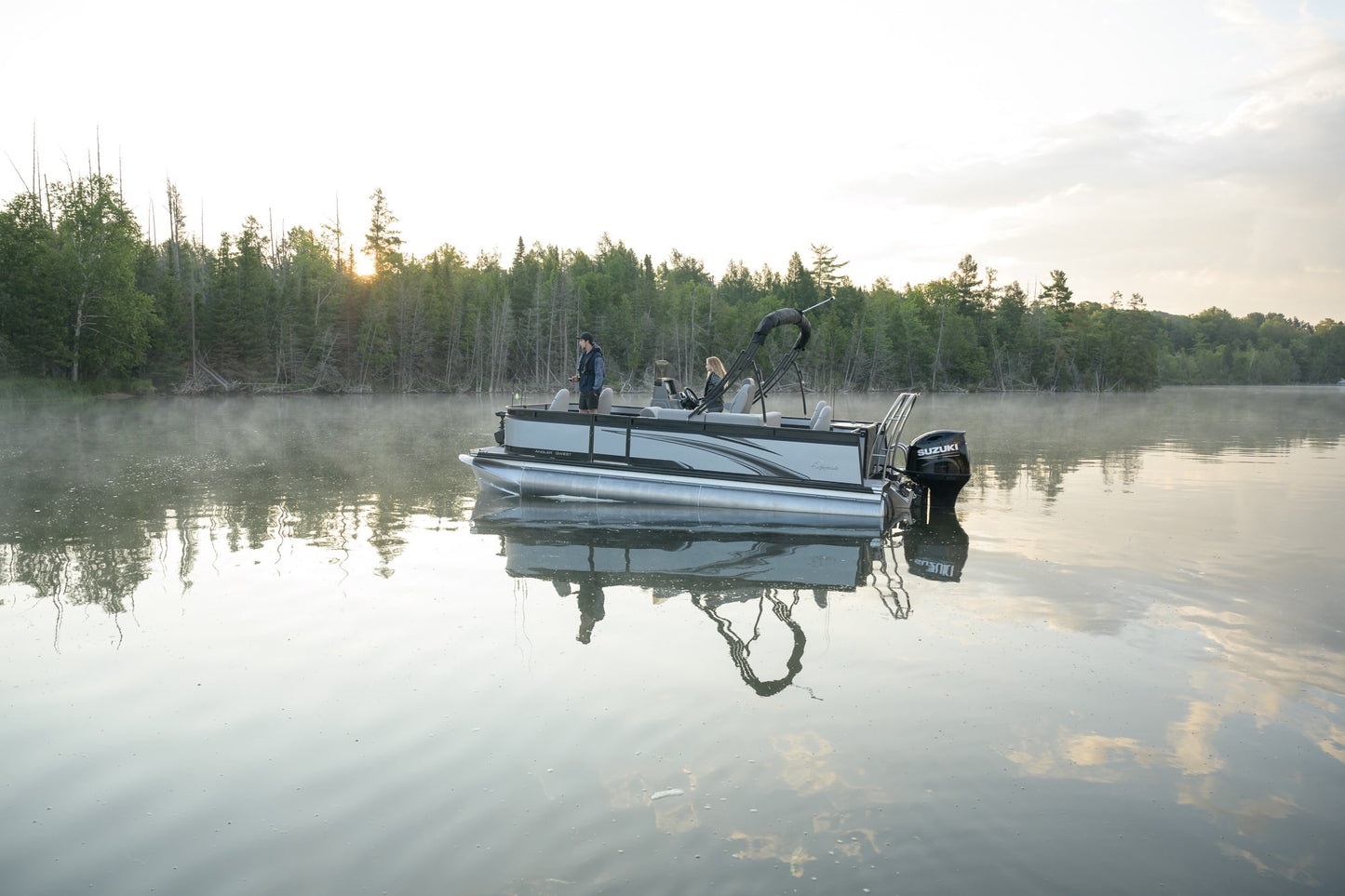 Pond with a pontoon boat and people on a misty morning