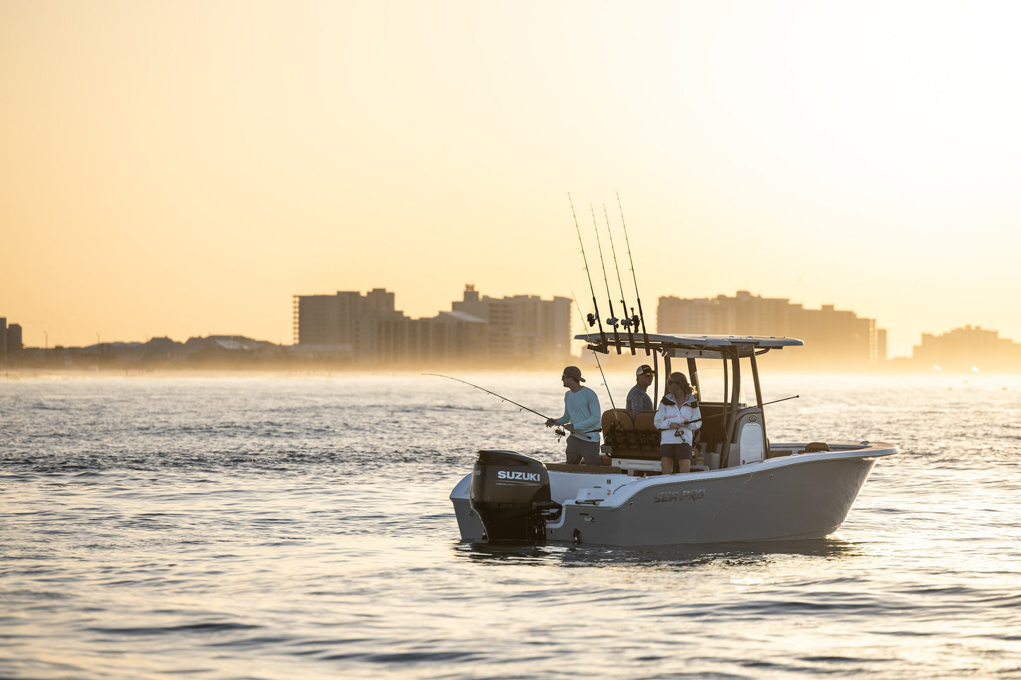 Fishing boat on the water with a city skyline in the background during sunset.