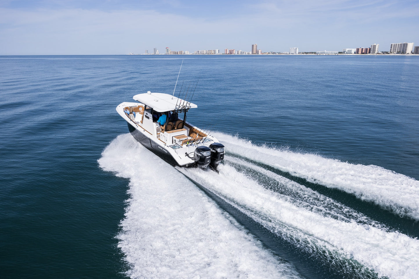 White boat speeding with Twin Suzuki 350 on a clear blue ocean with a city skyline in the distance